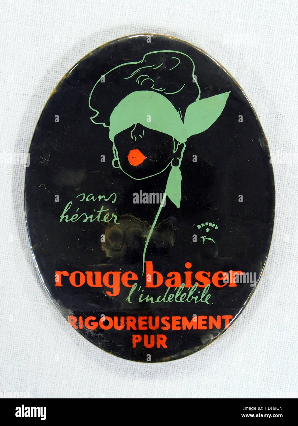 Die *Rouge Baiser* reklamespiegeltje ist ein alter Blechbehälter, der zur Aufbewahrung von Keksen oder Zigaretten verwendet wird und oft mit Vintage-Werbung in Verbindung gebracht wird. Sein Design spiegelt die kommerzielle Ästhetik des frühen 20. Jahrhunderts wider. Stockfoto