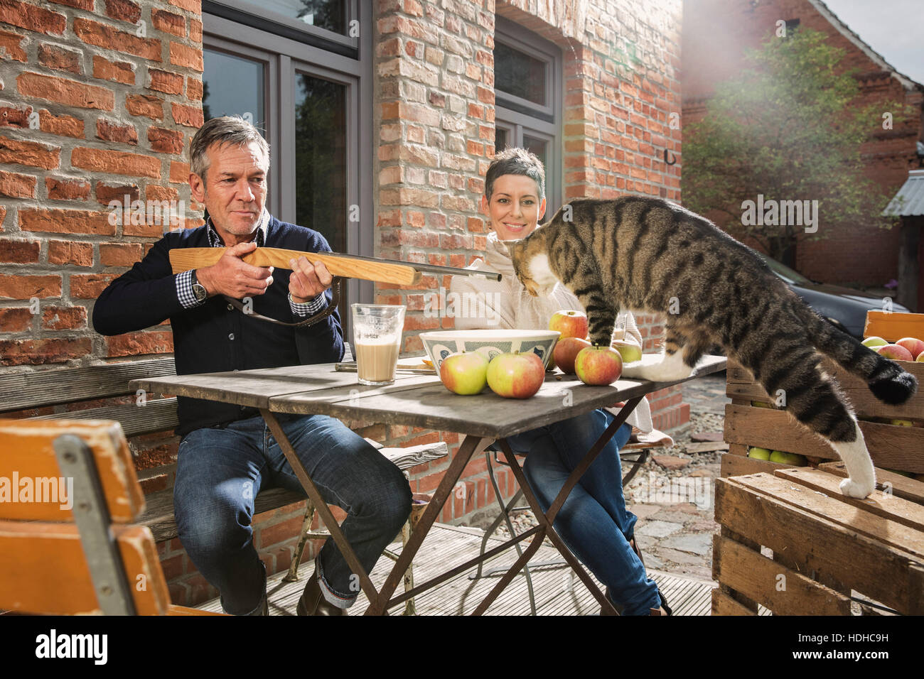 Spielerische Mann, mit dem Ziel Spielzeug Gewehr auf Tabby Katze sitzend mit Frau im Hinterhof Stockfoto