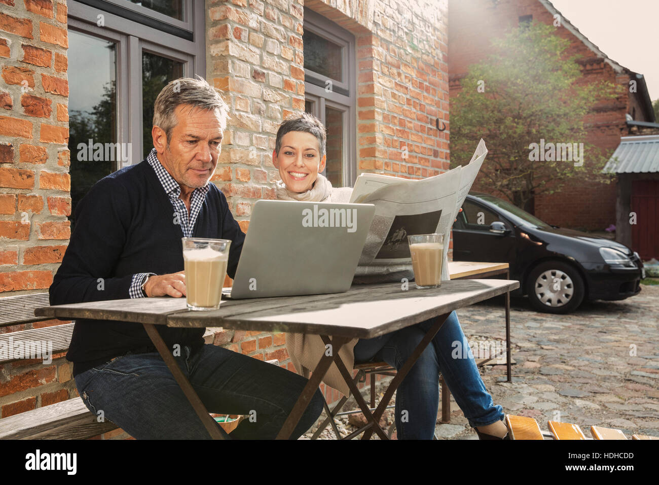 Reifer Mann mit Laptop mit Frau mit Zeitung im Hinterhof Stockfoto