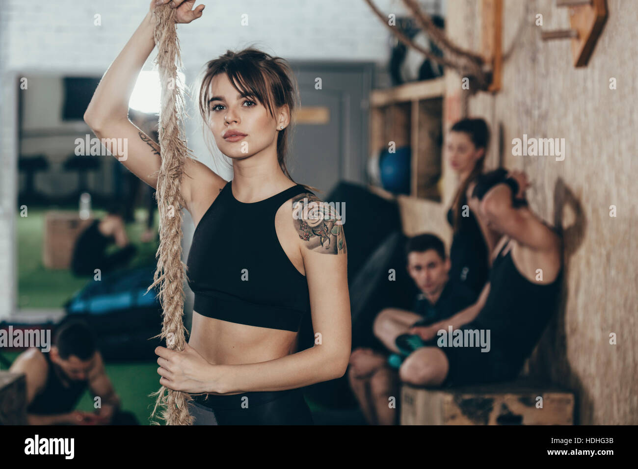 Porträt von zuversichtlich Sportlerin halten Seil stehend im Fitnessstudio mit Freunden im Hintergrund Stockfoto