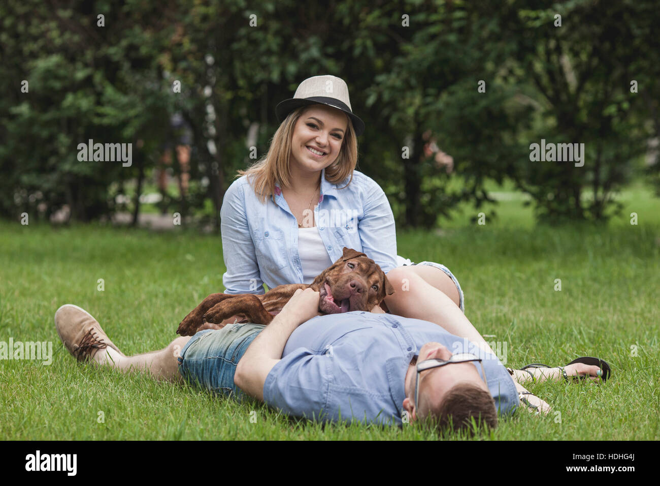 Ein Mann mit seinem Hund auf ihm liegend, während seine Freundin von ihm entspannt schlafen Stockfoto