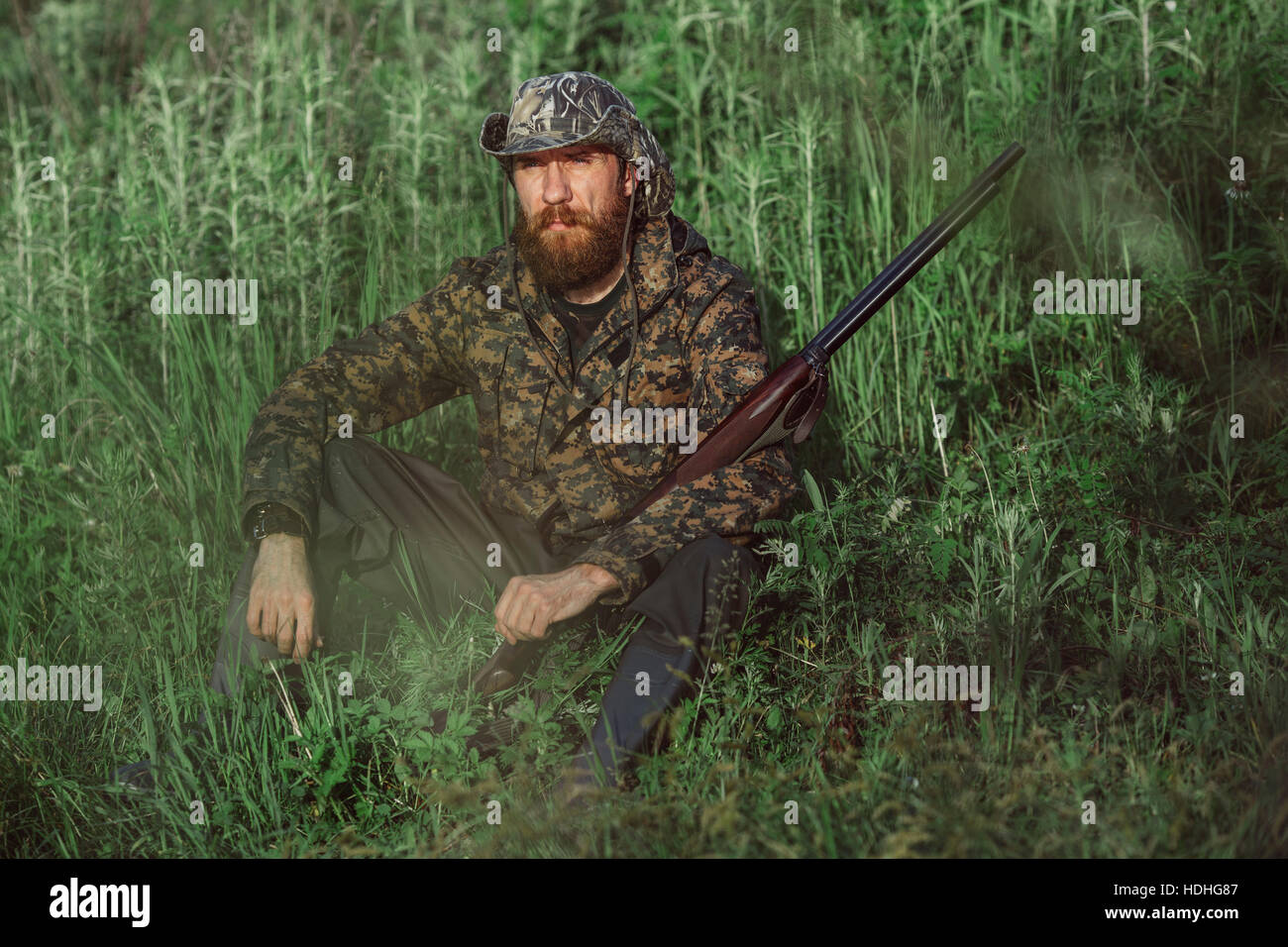 Jäger Holding Gewehr sitzend auf Wiese Stockfoto