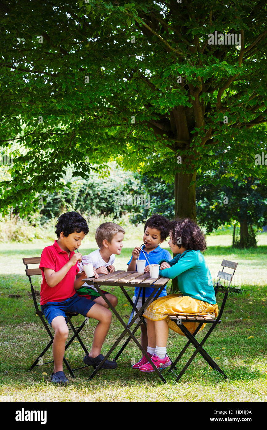Vier Kinder sitzen um einen Tisch auf einer Wiese. Stockfoto