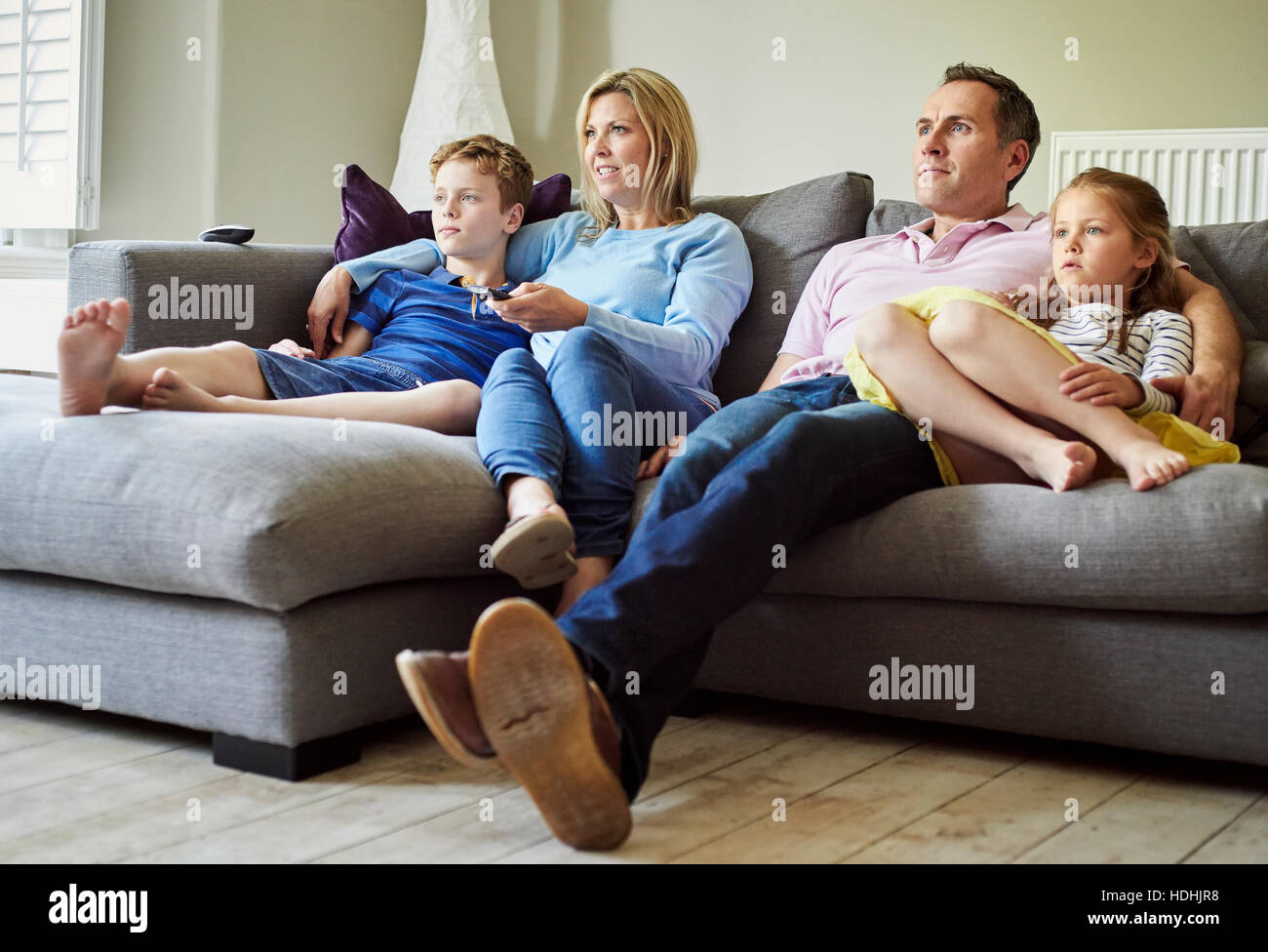 Eine Familie von vier Personen, Eltern und ein Mädchen und jungen, sitzen auf dem Sofa zusammen, vor dem Fernseher. Stockfoto