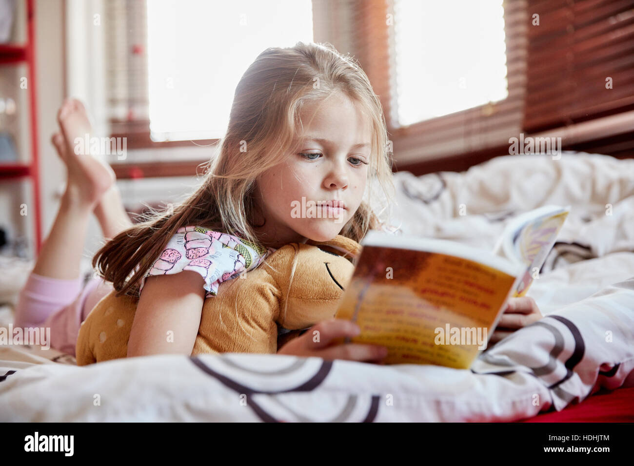 Ein Mädchen auf dem Bett auf den Bauch liegend ein Buch lesen. Stockfoto