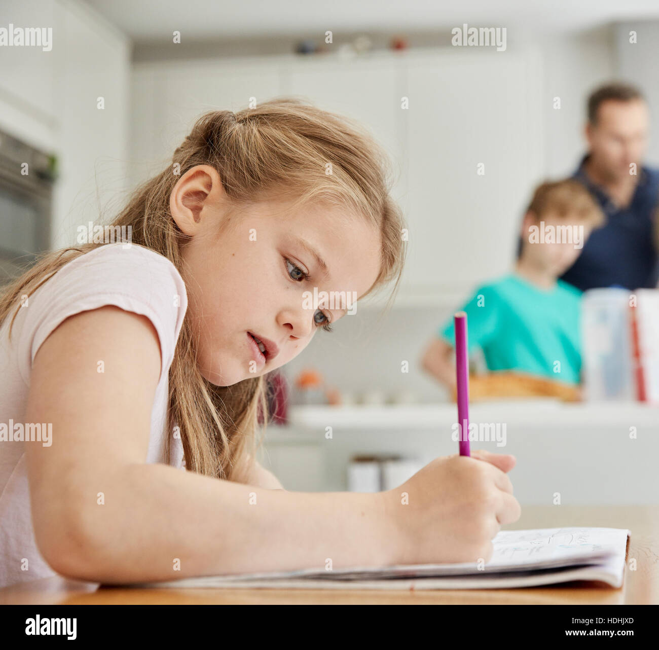 Ein Mädchen sitzt an einem Tisch in der Küche der Familie, mit einem Bleistift ihre Hausaufgaben. Stockfoto