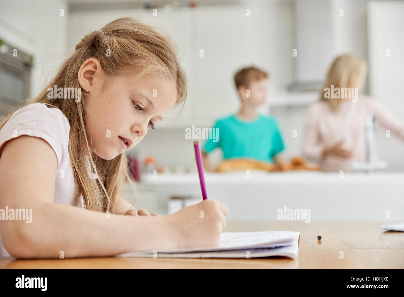 Ein Mädchen sitzt an einem Tisch in der Küche der Familie, mit einem Bleistift ihre Hausaufgaben. Stockfoto