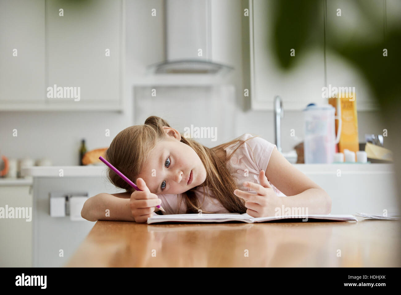 Ein Mädchen sitzt an einem Tisch in der Küche der Familie, einen Bleistift, mit dem Kopf in ihren Händen halten. Stockfoto