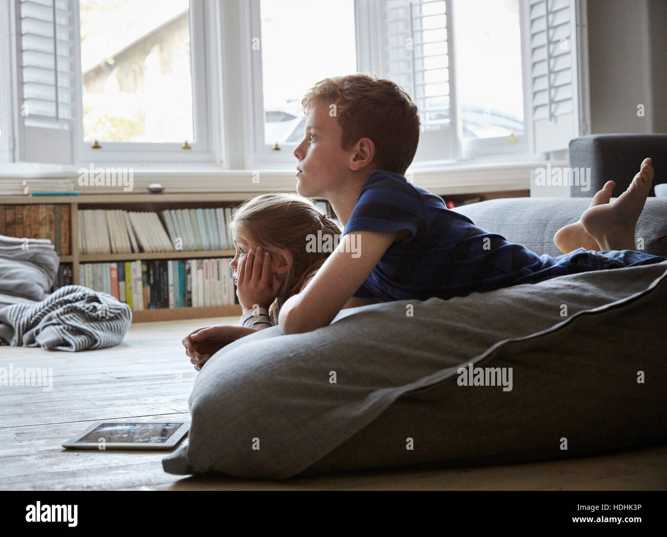 Eine Familie zu Hause. Zwei Kinder auf dem Boden liegend vor dem Fernseher. Stockfoto