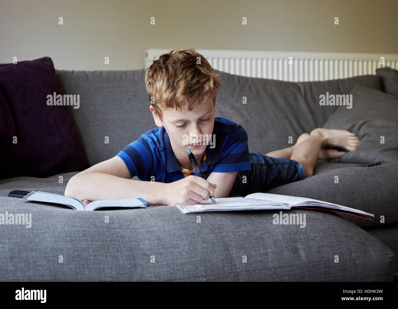 Eine Familie zu Hause. Ein Junge liegt auf seiner Vorderseite auf dem Sofa seine Hausaufgaben in ein Heft schreiben. Stockfoto