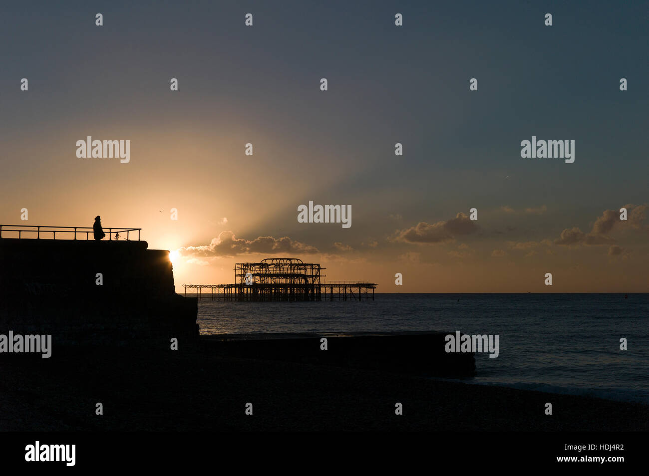 Abbildung silhouettiert gegen aufgehende Sonne hinter Buhne, Brightons verlassenen West Pier im Hintergrund Stockfoto