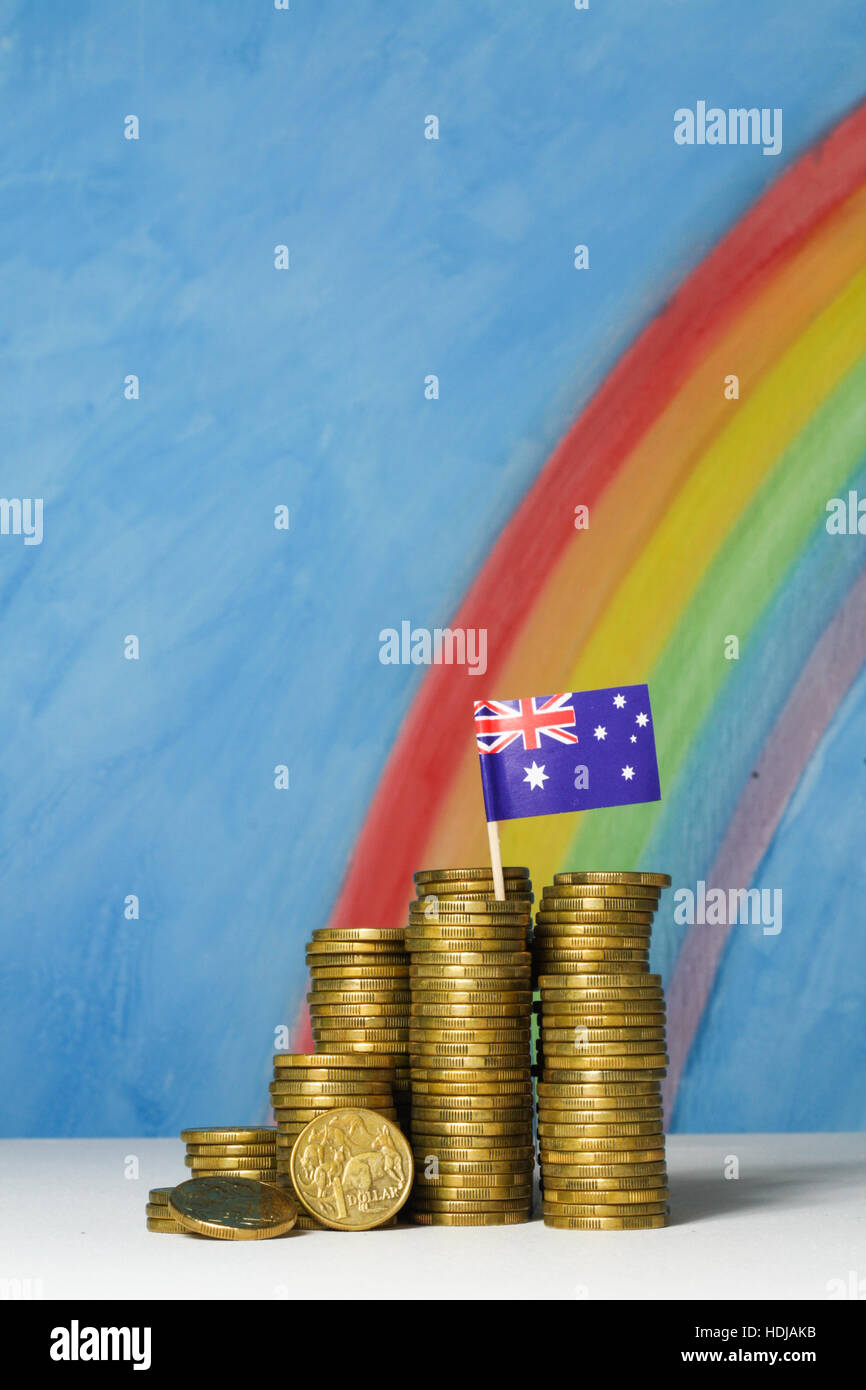 Gold-Dollar-Münzen und australische Flagge vor einem blauen Himmel und Regenbogen Hintergrund, veranschaulicht das Konzept von Devisen. Stockfoto