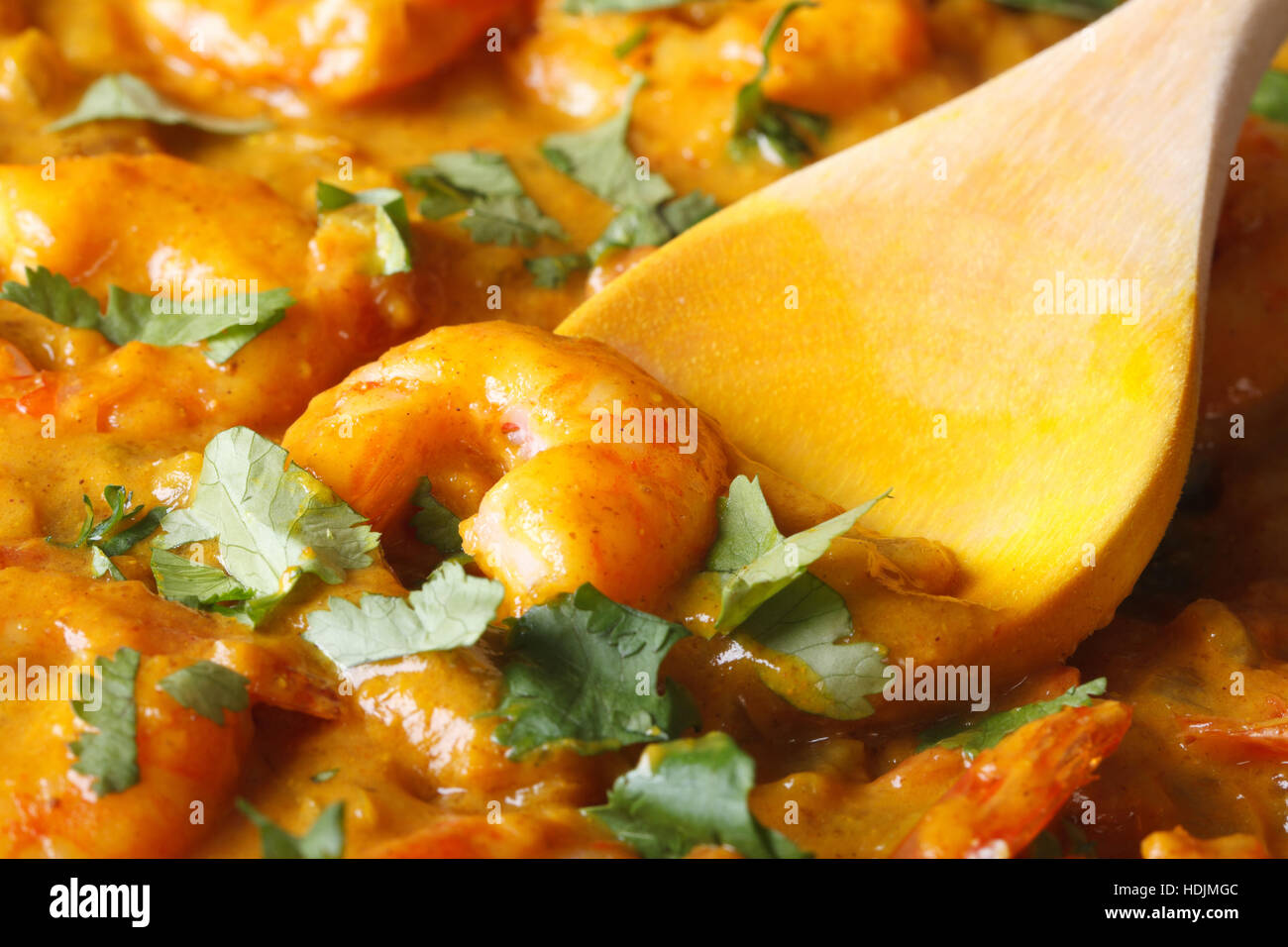 Garnelen in Curry-Sauce mit Koriander und Holzlöffel Makro. horizontale Stockfoto