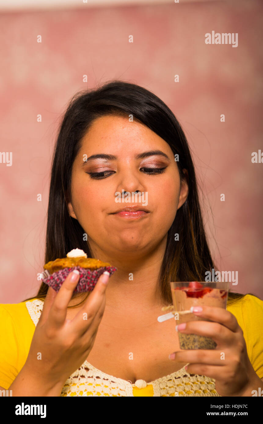 Brünette Frau mit köstlichen braunen farbigen Muffin mit Sahne-topping, Glas Mousse in der anderen Hand, Lächeln und bereit, ein Biss, Gebäck-Konzept Stockfoto