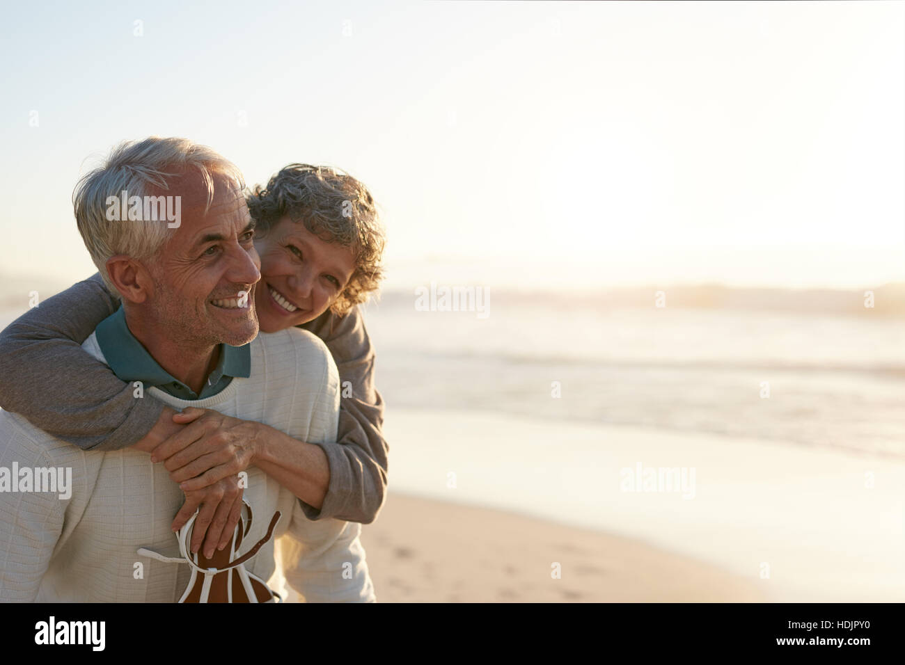 Porträt von glücklich reifer Mann wird von seiner Frau am Strand umarmt. Älteres Paar, die Spaß am Ufer Meeres. Stockfoto