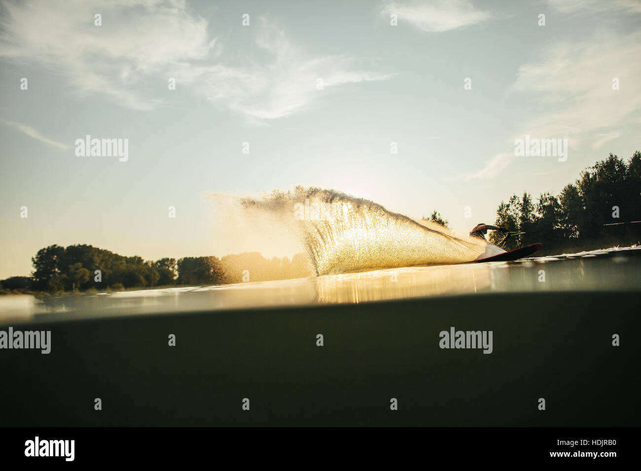 Wasserschifahrer bewegt sich schnell in Spritzwasser bei Sonnenuntergang. Mann Wakeboarden auf einem See Stockfoto