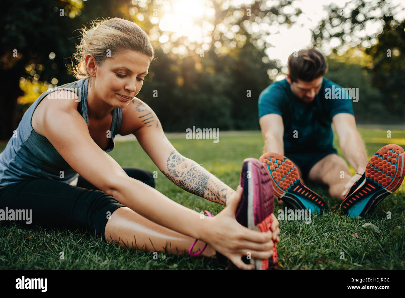 Schöne junge Frau mit Mann im Hintergrund dehnen. Kaukasische paar gemeinsam Morgengymnastik im Park. Stockfoto