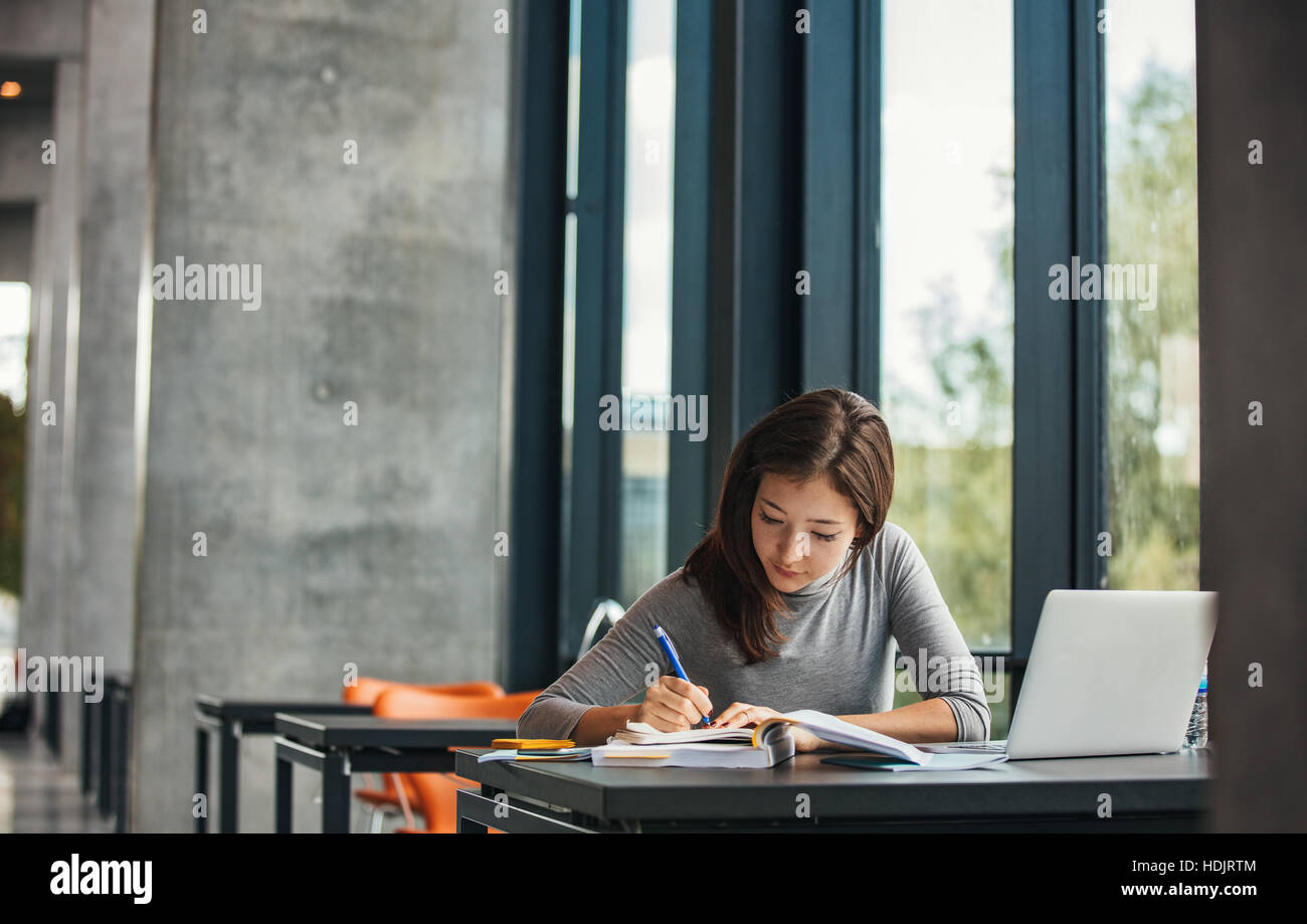 Schuss an junge asiatische Studentin am Tisch sitzen und schreiben am Notebook. Junge Studentin in der Bibliothek zu studieren. Stockfoto