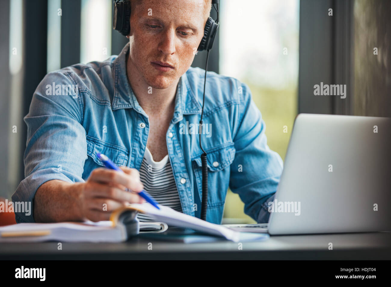 Aufnahme des jungen männlichen Studenten Buch zu lesen, während Sie am Tisch sitzen. Mann mit Laptop Buch am College-Bibliothek. Stockfoto