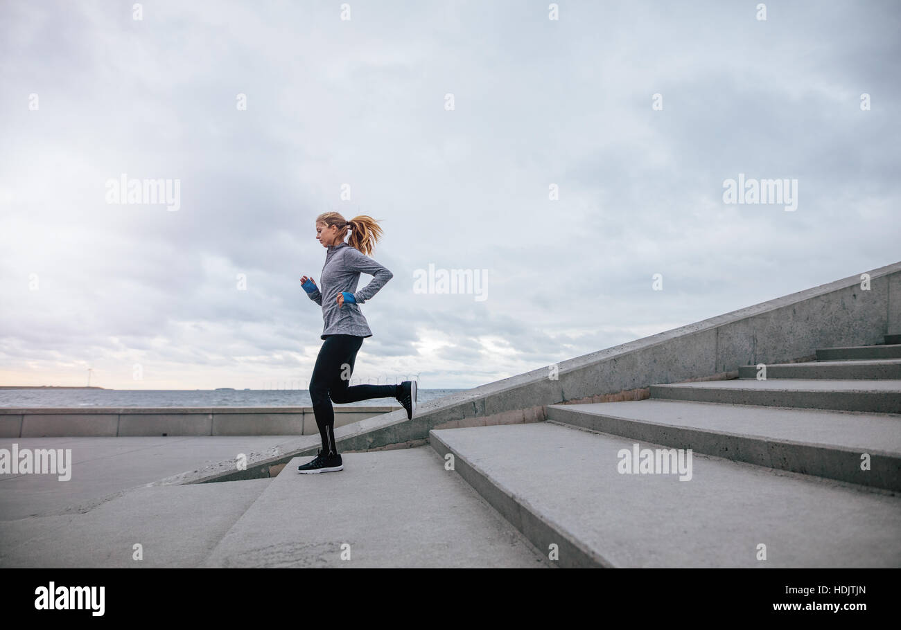 Volle Länge einer gesunden jungen Frau, die die Stufen hinunterläuft. Fitnesstraining für Frauen am Morgen im Freien. Stockfoto