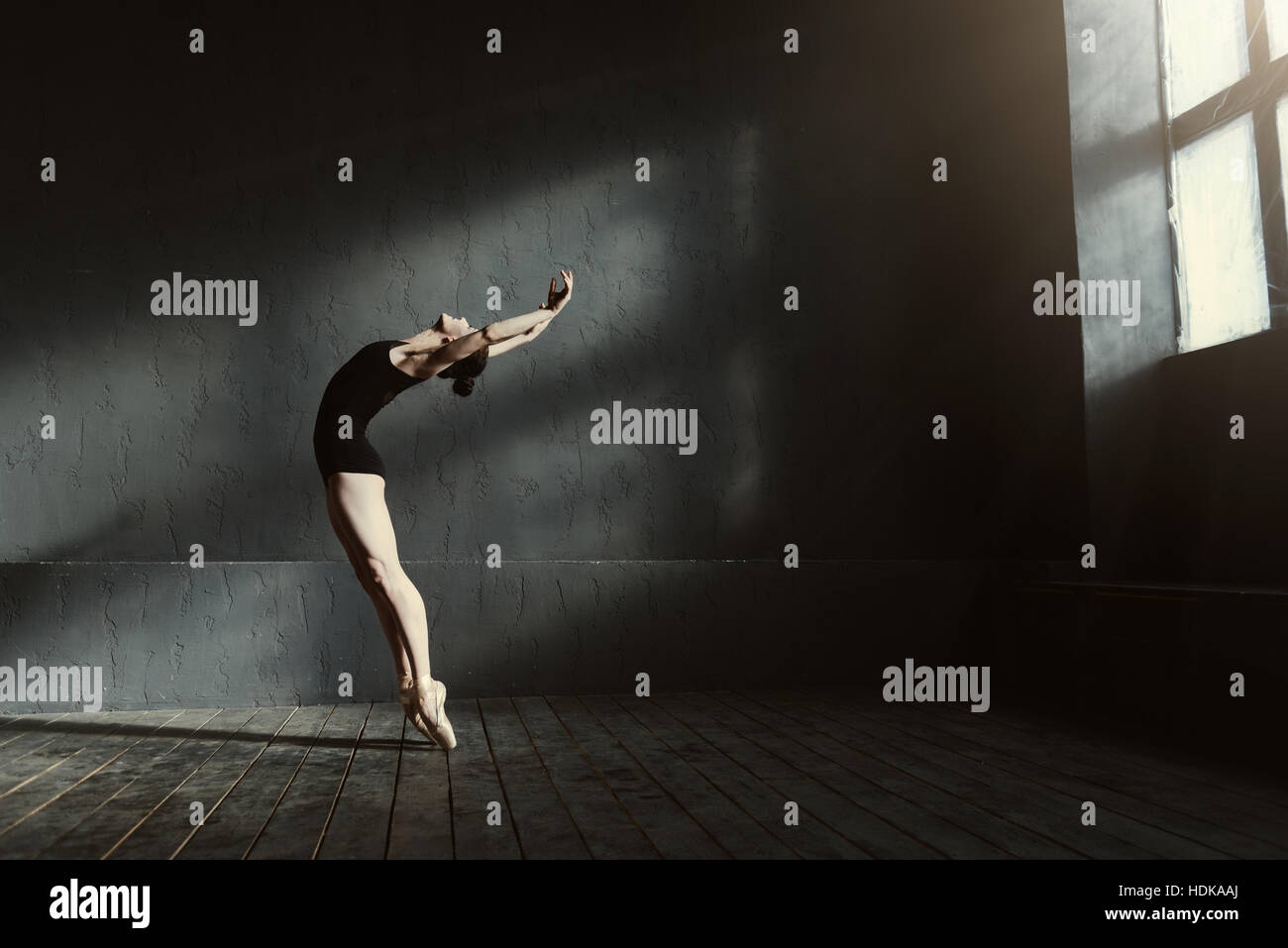 Flexible Ballett-Tänzerin im dunklen beleuchteten Studio dehnen Stockfoto