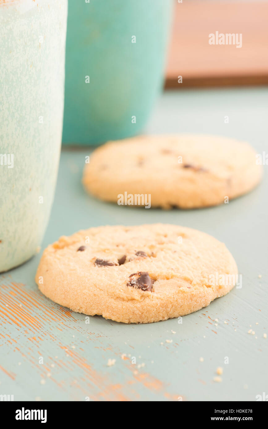 Chocolate Chip Cookies und Kaffee oder Tee Tassen. Süße Speisen, Nachtisch oder Snack. Die Cookies werden auf einem Küchentisch serviert. Stockfoto