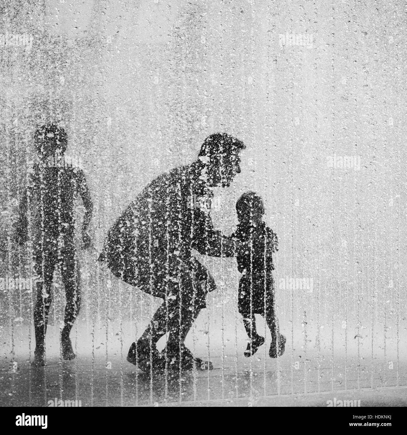 Silhouette der ein kleiner Junge, ein Mann und ein Kleinkind in einem Springbrunnen spielen. Stockfoto