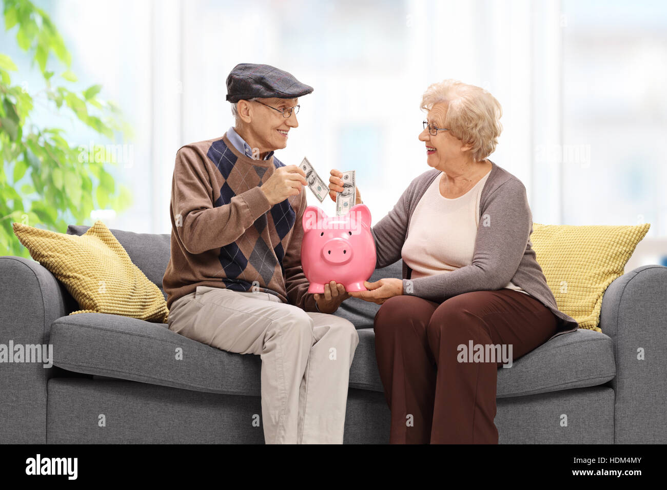 Senioren auf dem Sofa sitzen und Geld in ein Sparschwein Stockfoto