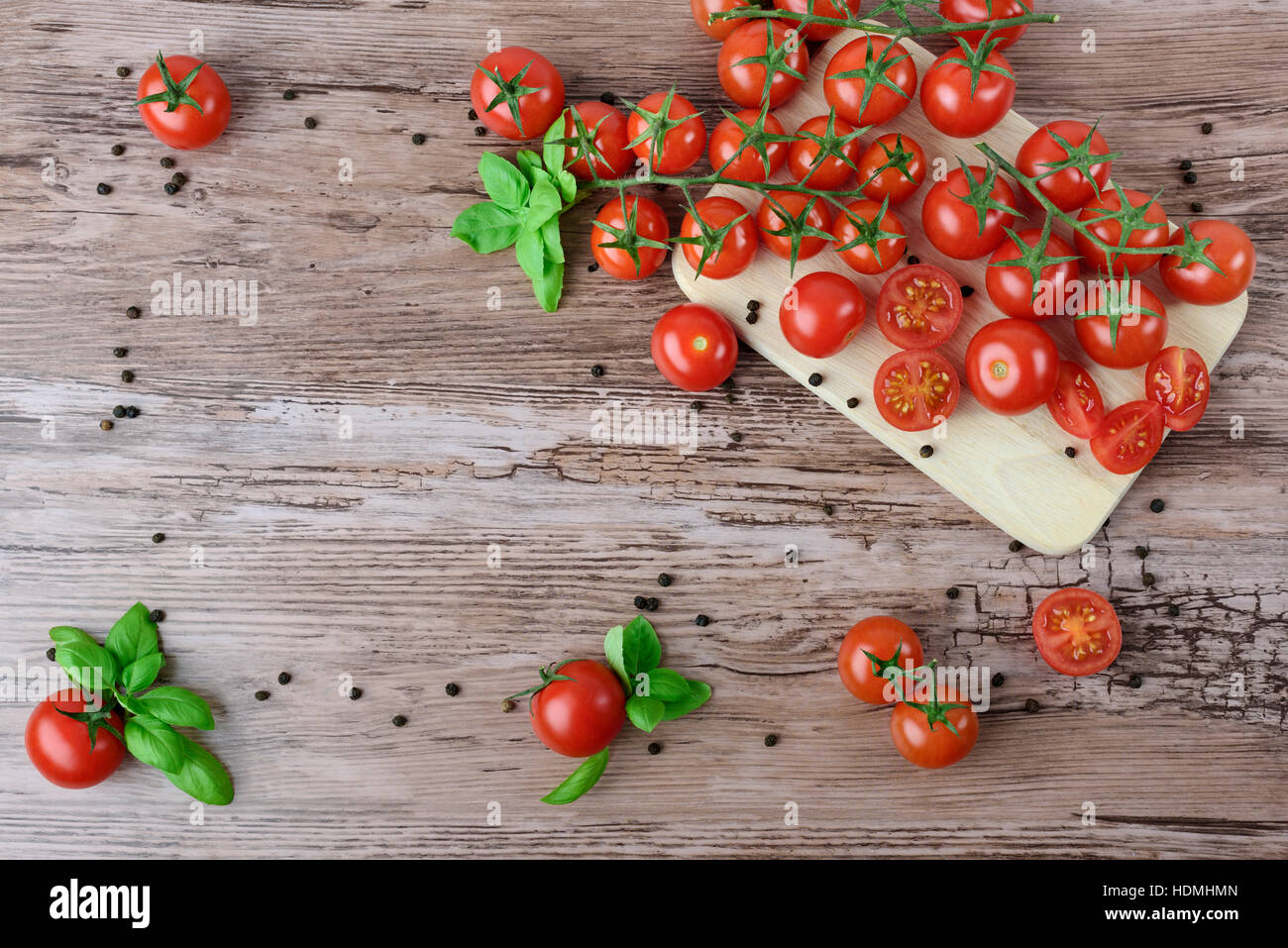 Tomaten und Paprika in Gruppen mit Blättern Basilikum auf dem braunen Holztisch. Stockfoto