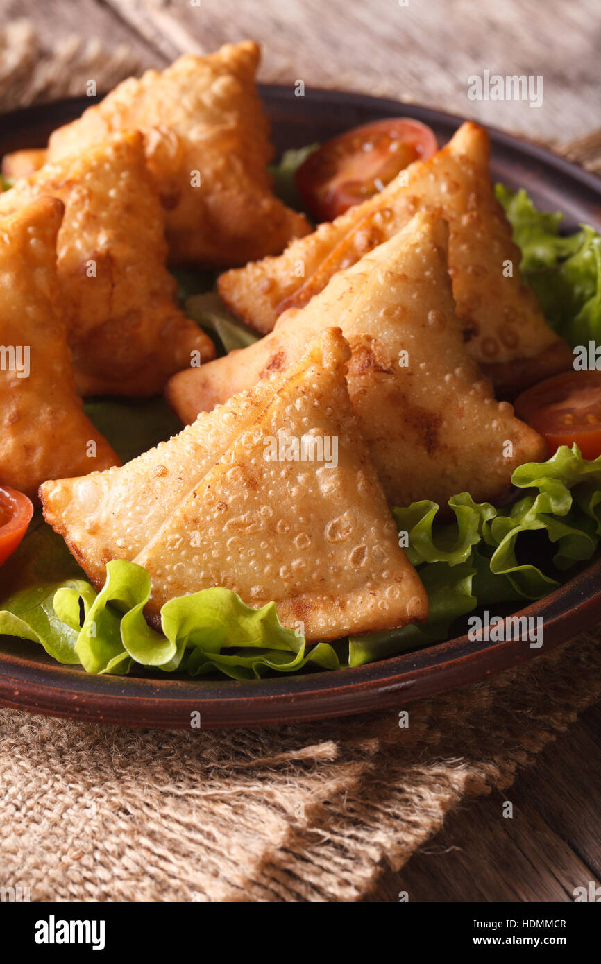 Samosa auf einem Teller mit Tomaten und Salat auf einem Holztisch. Vertikale Nahaufnahme Stockfoto