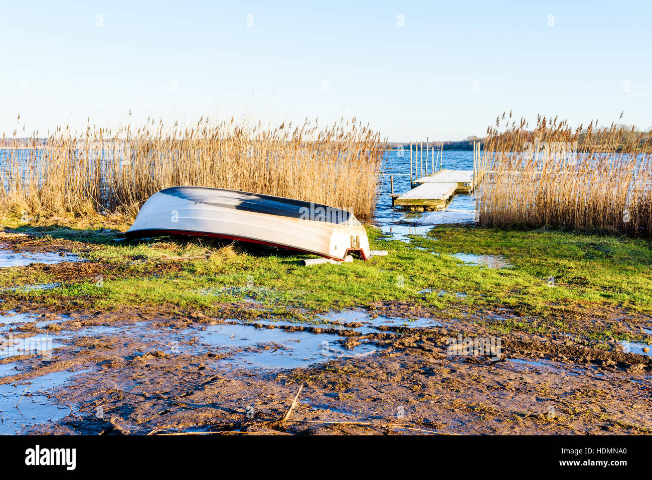 Umgestürzten kleines Ruderboot auf dem Land an einem frostigen und kalten Morgen im Winter. Eis bedeckt Pfützen umgeben das Boot. Frostigen Holzmole in Öffnung sichtbar Stockfoto