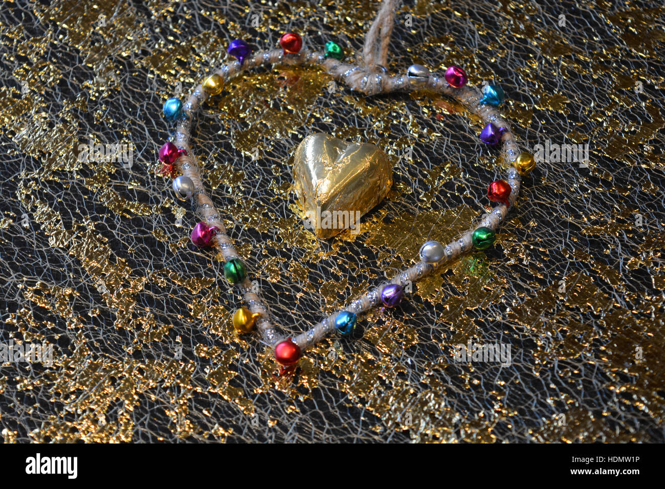 Goldfolie überzogen Schokoladenherz, umgeben von einer Herzform mit Glocken Stockfoto