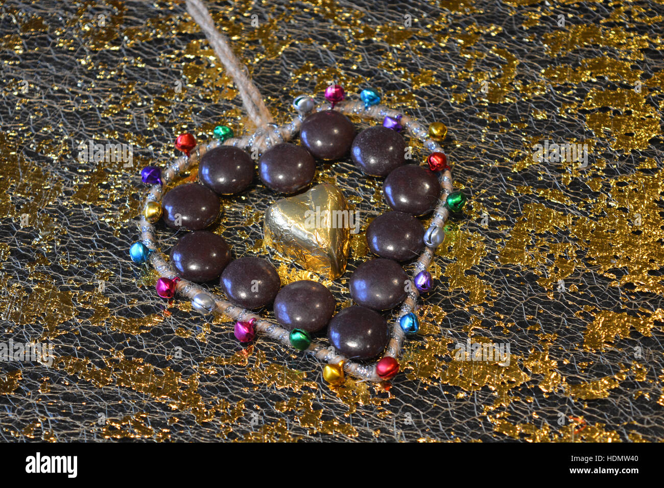 Goldfolie überzogen Schokoladenherz umgeben von Schokolade Tropfen und eine Herzform mit Glocken Stockfoto