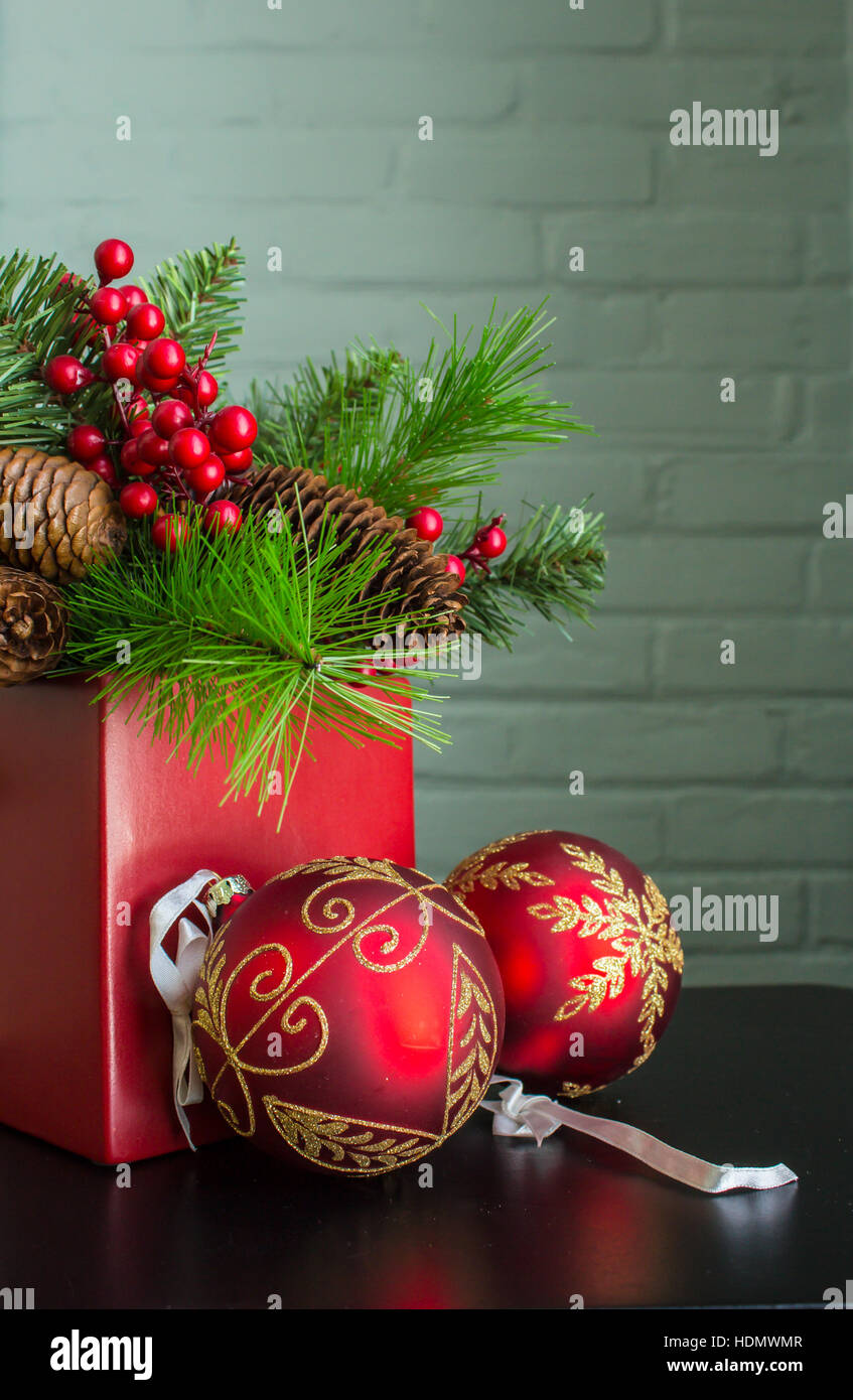 Immergrün, Beeren und Zapfen in einem leuchtend roten Topf mit aufwendigen dekorativen Weihnachtsschmuck. Stockfoto