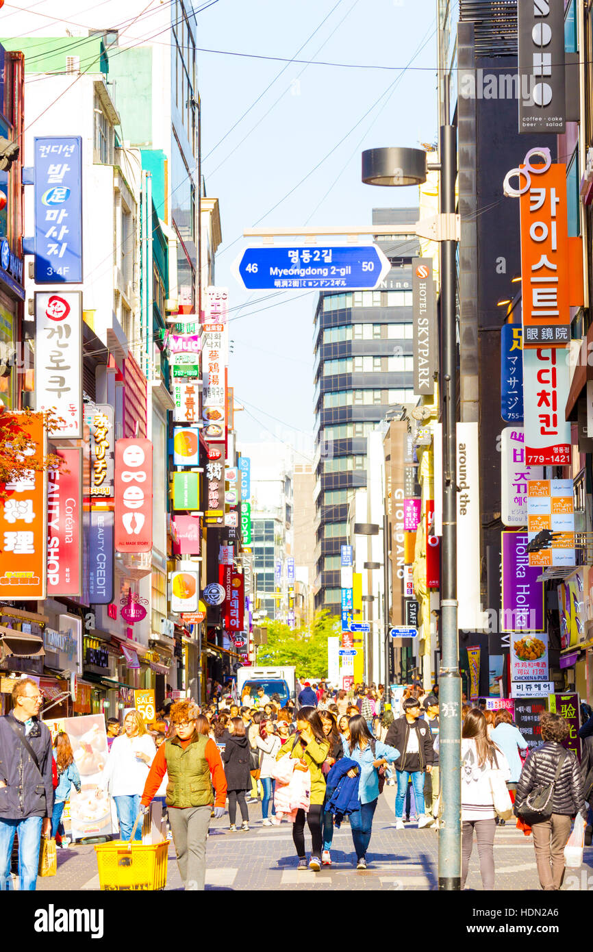Touristen zu Fuß hinunter belebten Myeongdong Fußgängerzone umgeben von Kommerzialisierung des speichert, Zeichen und überfüllt Stockfoto