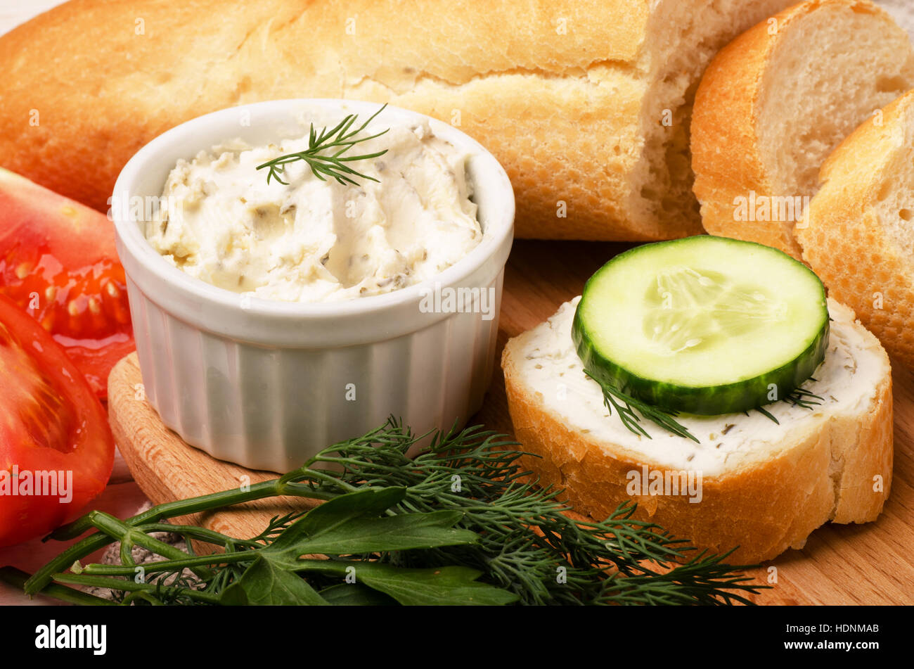 Knusprige Baguette Scheiben mit Frischkäse mit Kräutern und Gemüse auf Schneidebrett zum Frühstück Stockfoto