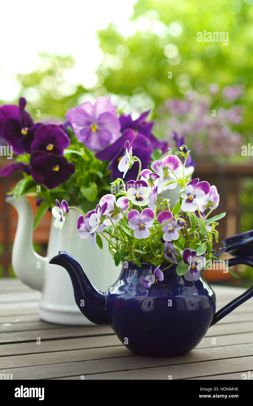 Lila Stiefmütterchen Blumensträuße in blauen und weißen Emaille-Kannen über einen Balkon mit Tisch, Kopie oder Text Raum, nostalgischen Hintergrund Stockfoto