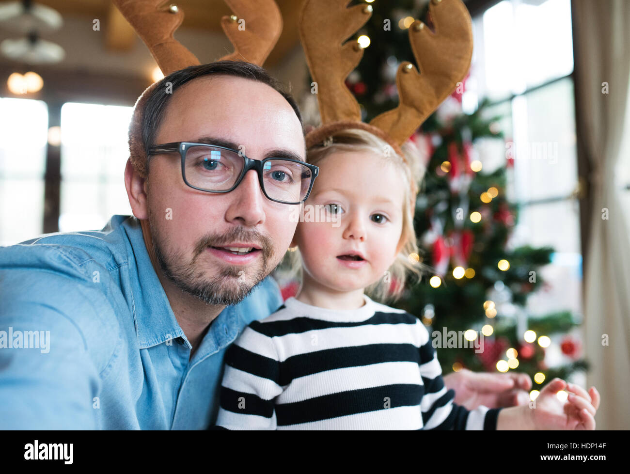 Vater mit stahlharte am Weihnachtsbaum, Rentier-Geweih tragen Stockfoto
