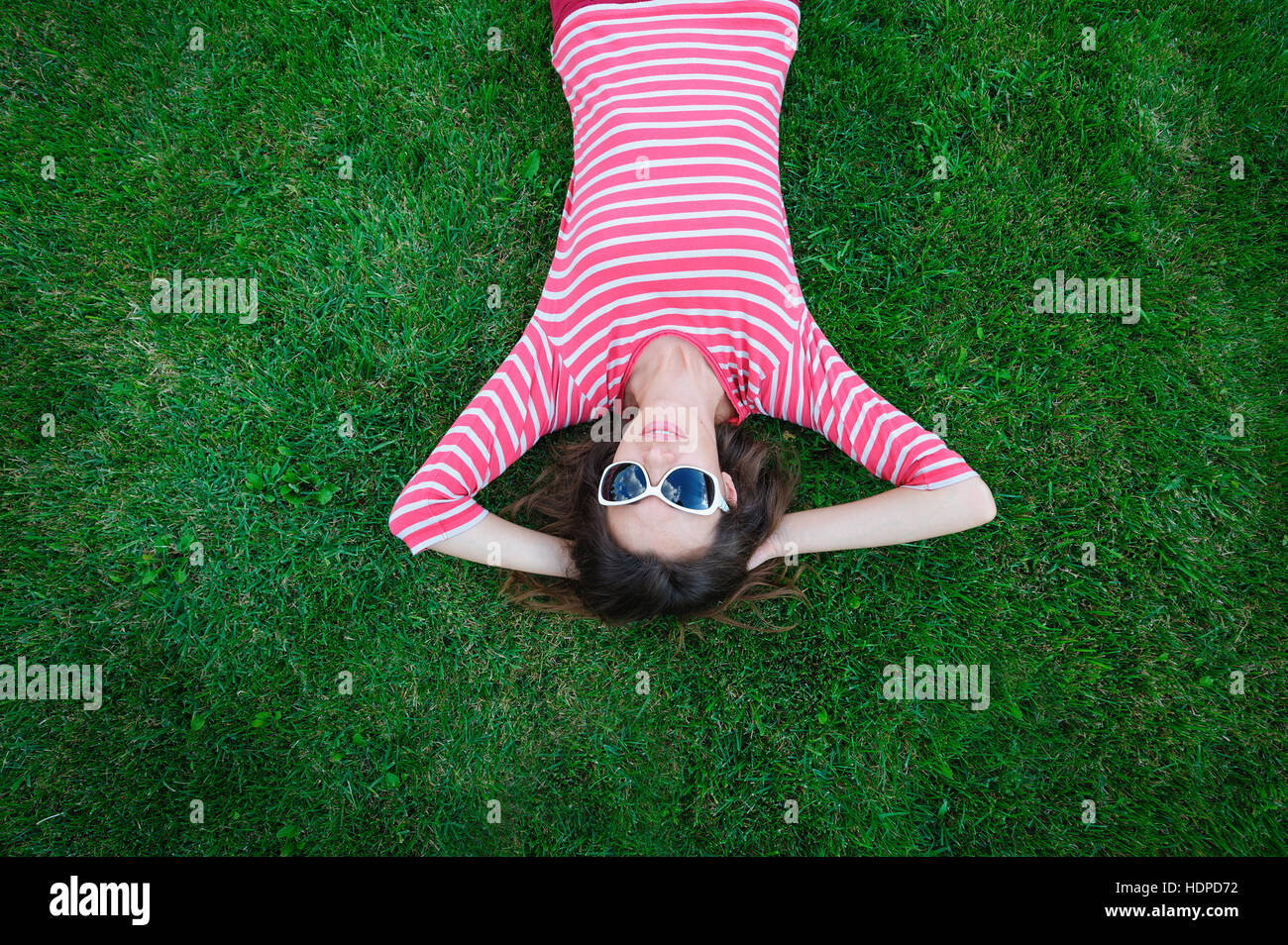 schöne junge Frau, die auf dem grünen Rasen auf der Wiese liegend Stockfoto