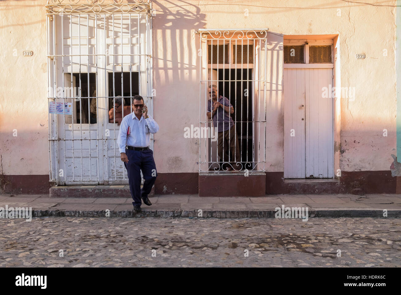 Mann auf dem Handy geht weg von Haus mit typischen vergitterten Fenstern in Trinidad, Kuba Stockfoto