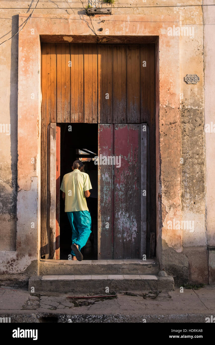 Mann betritt sein Haus durch eine alte hölzerne Eingangstür getaucht in warmes Sonnenlicht, Camagüey, Kuba Stockfoto