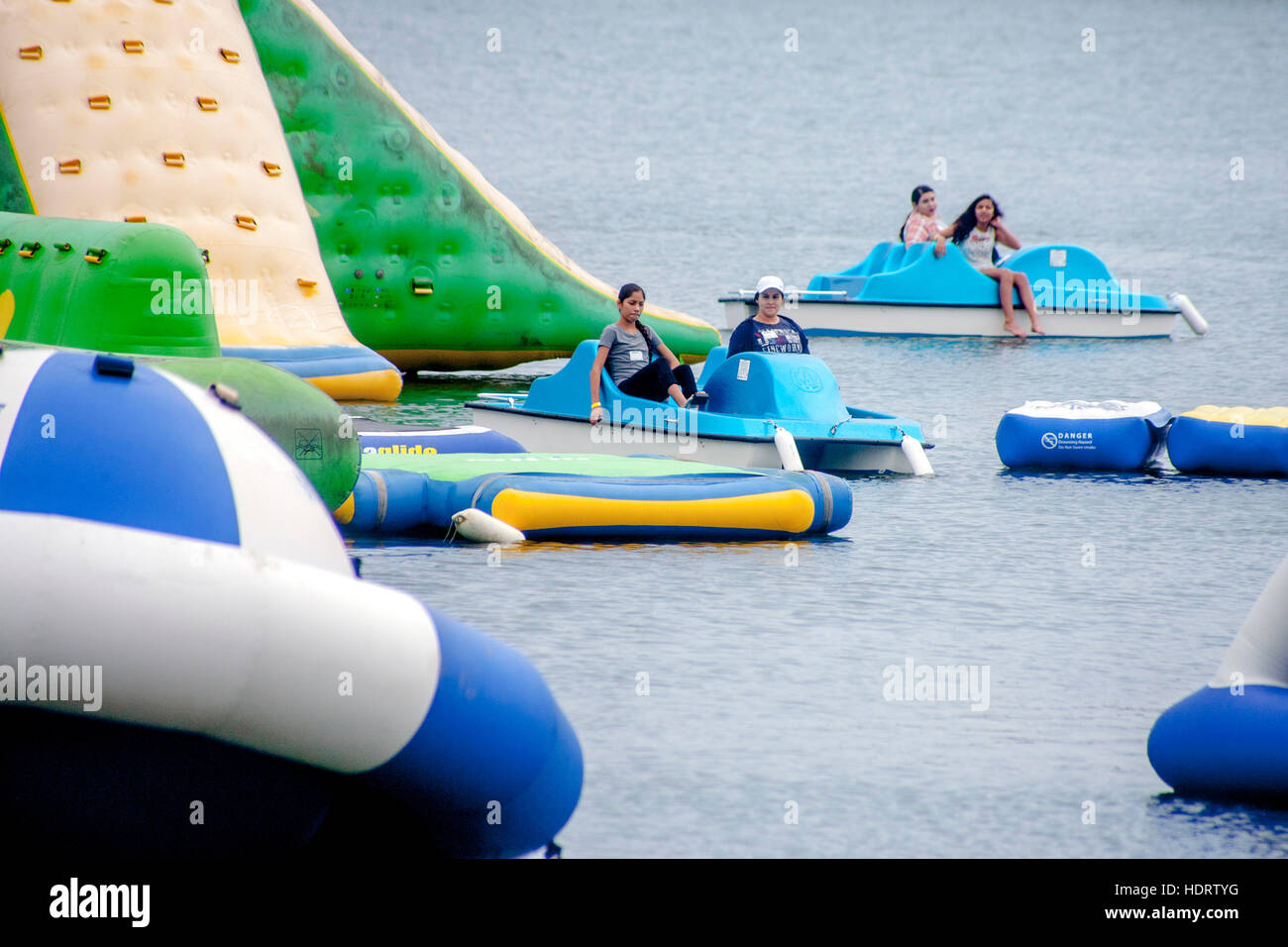 Gemischtrassig junge Erwachsene Steuern Tretboote durch einen Aquapark von bunten Schwimmern in Newport Beach, Kalifornien. Stockfoto