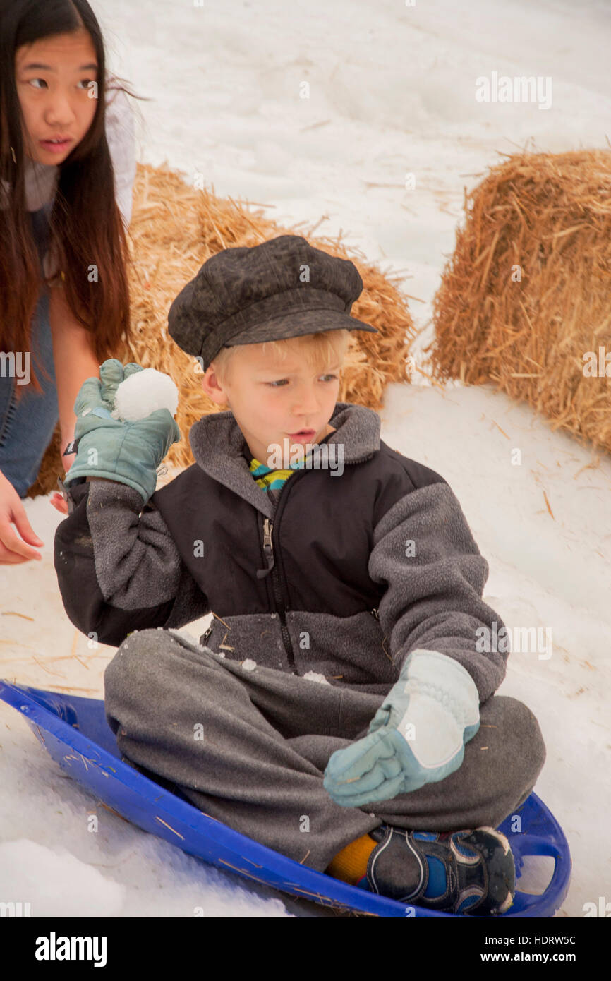 Sitzen auf einem Schlitten, wirft ein kleiner Junge einen Schneeball auf eine "Snowfest" Winter-Karneval mit Kunstschnee in Lake Forest, Kalifornien. Stockfoto