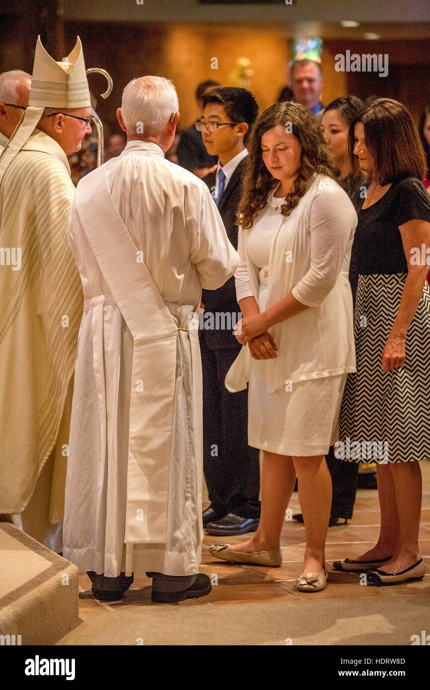 Von ihren Eltern begleitet, beteiligen formal gekleidete Jugendliche sich Bestätigung Messe in Laguna Niguel, CA, katholische Kirche vor einem wogenden Bischof. Stockfoto