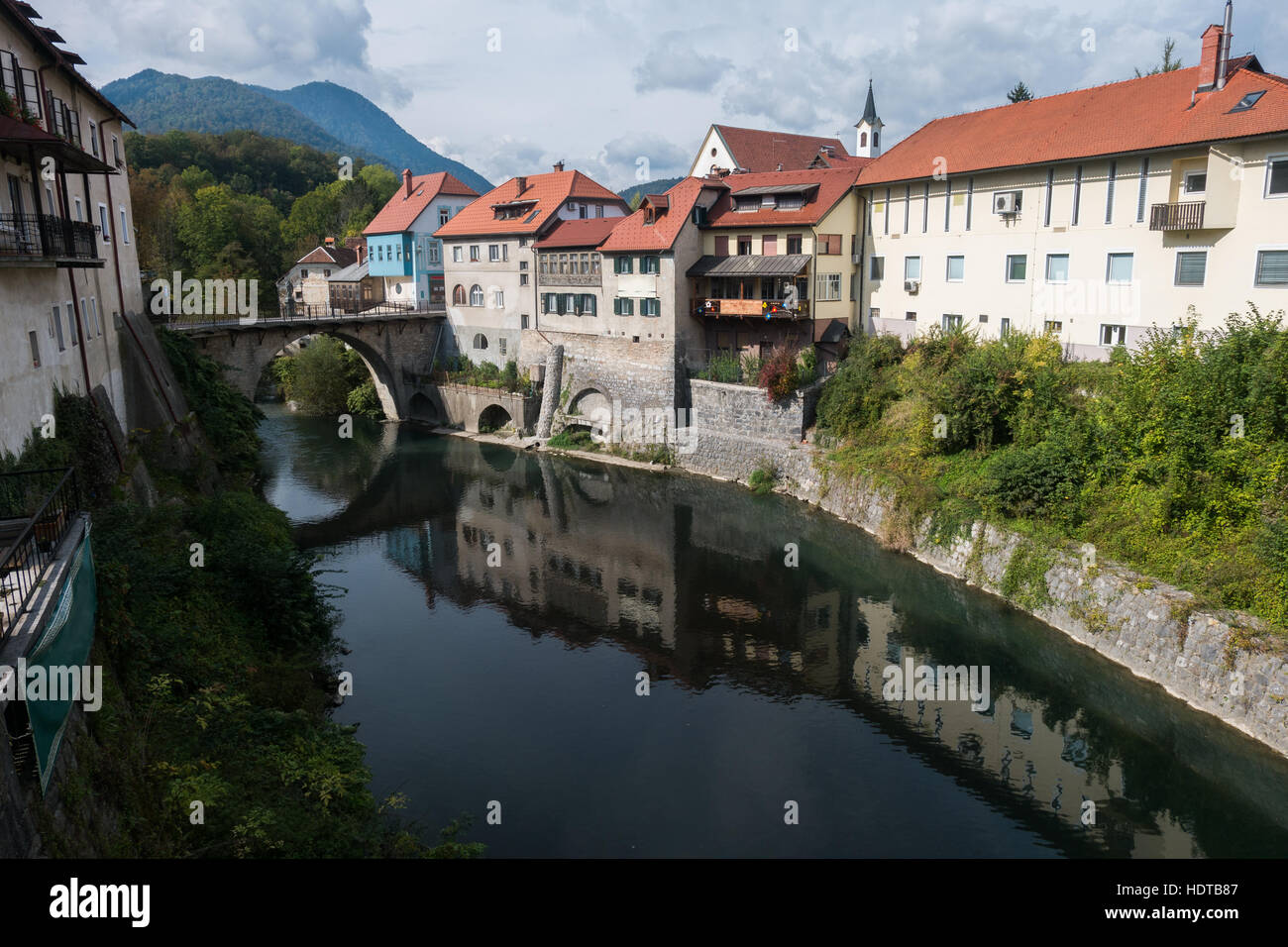 Fluss, der durch die historische Altstadt von Škofja Loka (Slowenien). Brücke über den Fluss und Reflexion von Gebäuden im Wasser. Stockfoto
