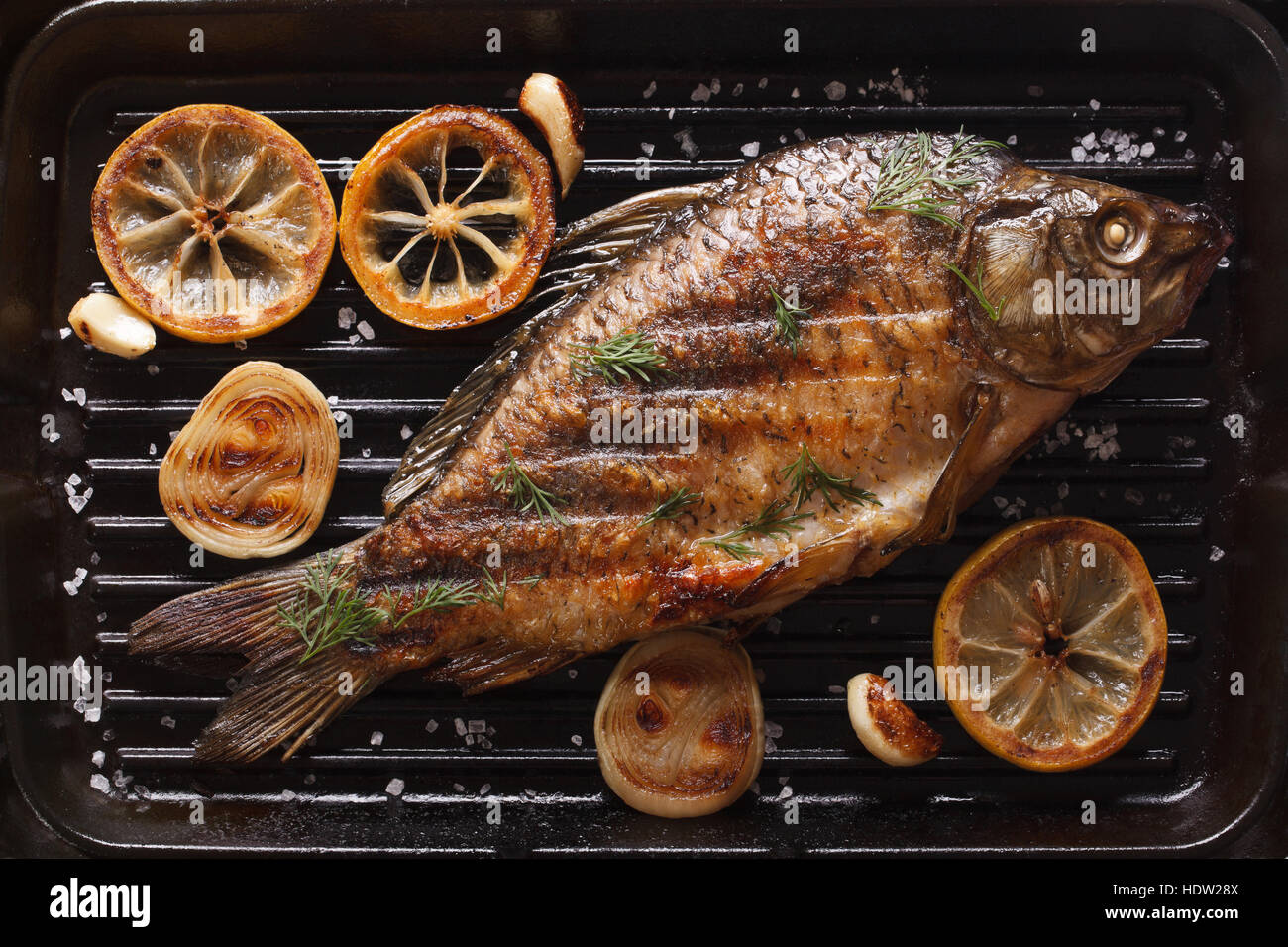 gebratene Karpfen mit Zitrone, Zwiebeln und Gewürze auf einem schwarzen Grill pan, horizontale Ansicht von oben, Nahaufnahme Stockfoto
