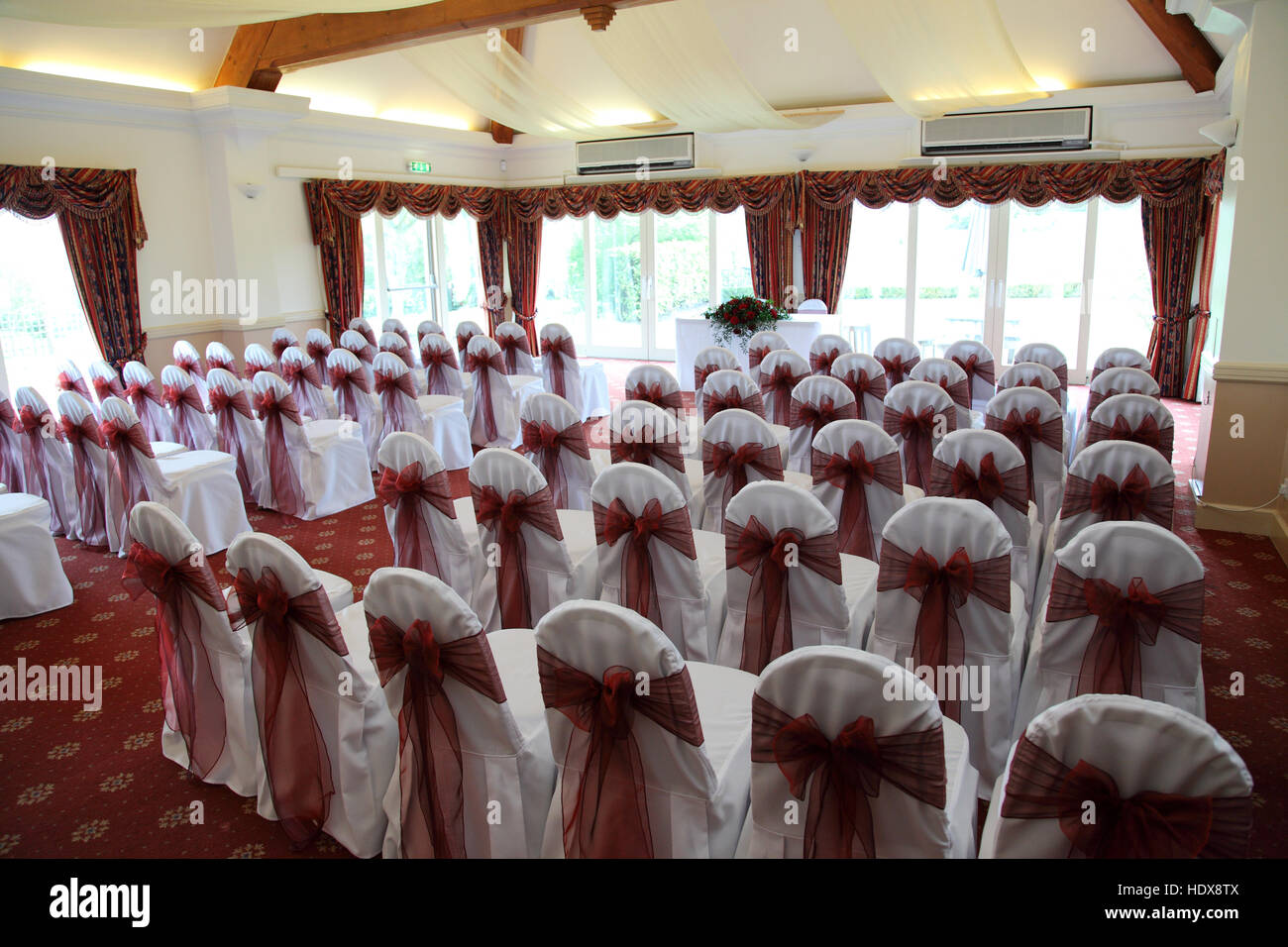 Ein Zimmer für eine standesamtliche Trauung, Stühle mit weißen Decken bereit gelegt und mit dunkel rosa Schleifen gebunden Stockfoto