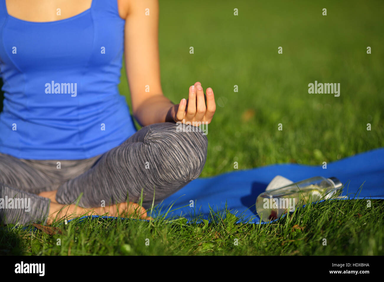 Junge Frau im blauen Hemd mit sitzt mit gekreuzten Beinen auf die Matte zu meditieren Stockfoto