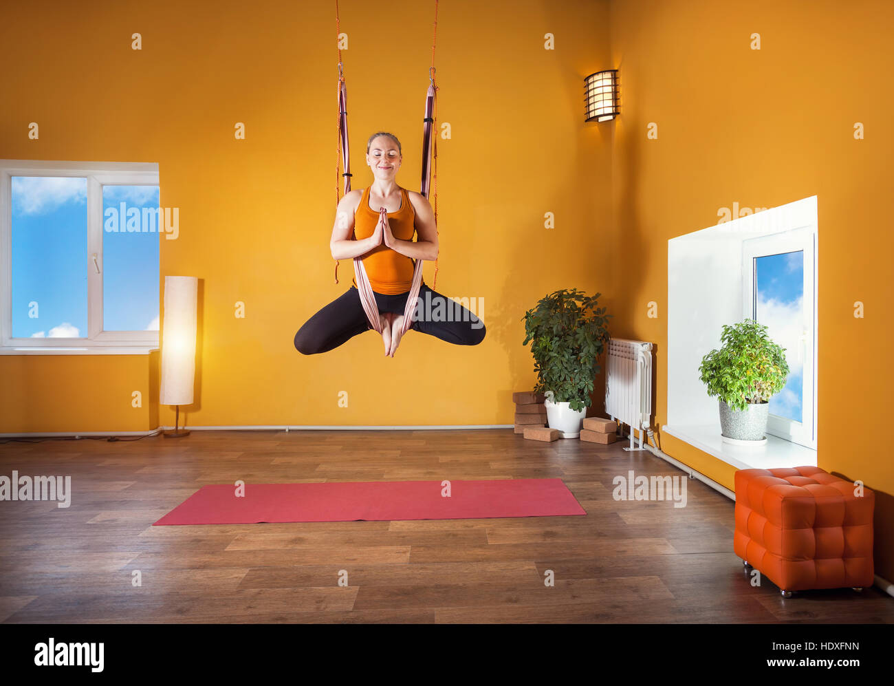 Junge Frau tut Antigravity Yoga meditativen Position im Studio mit gelben Wänden Stockfoto