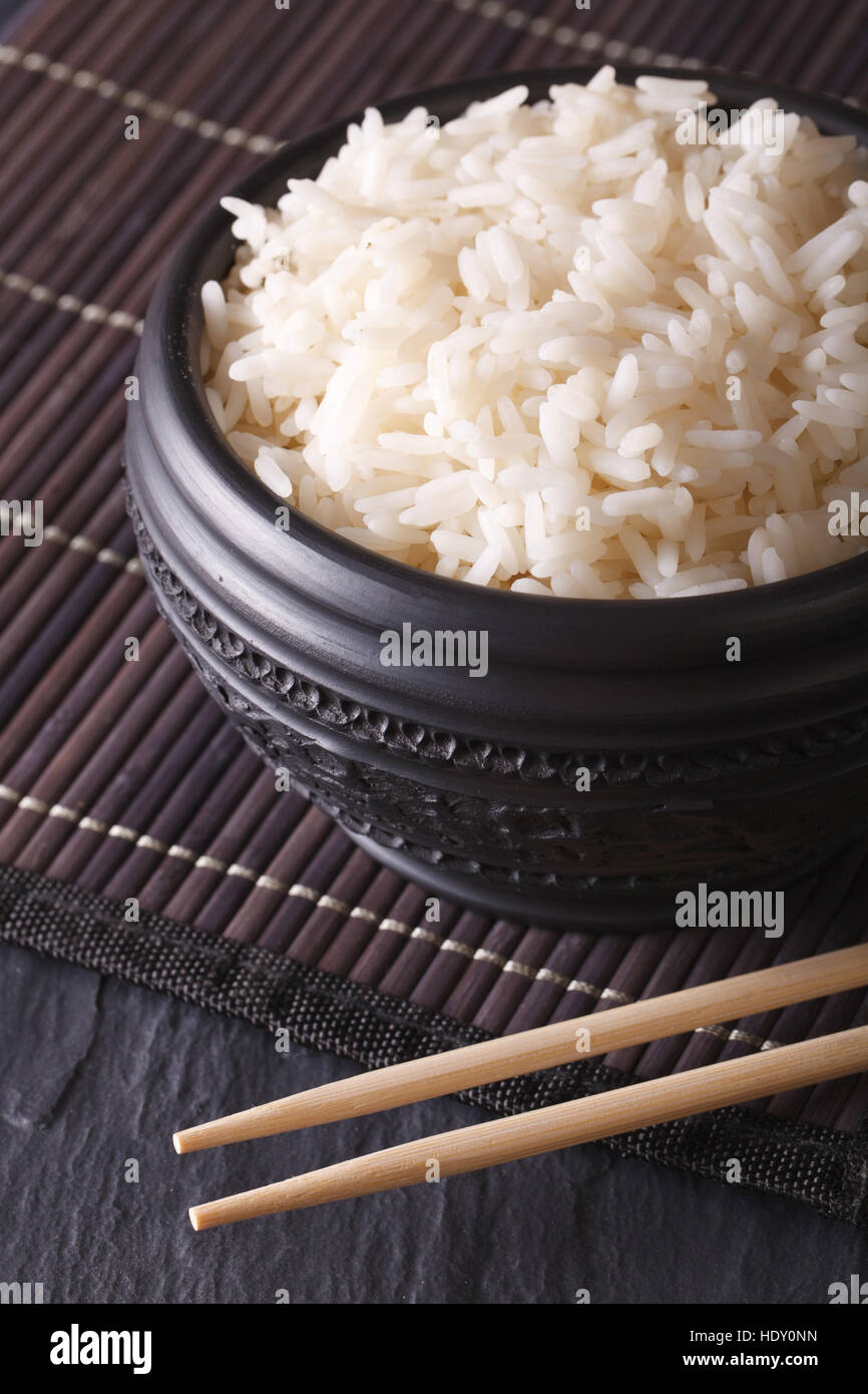 Asiatische Küche: gekochten Reis in eine schwarze Schale Nahaufnahme und Stäbchen. vertikale Stockfoto
